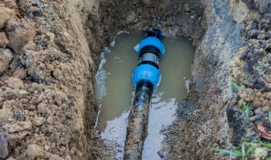 Irrigation repair showing a blue connector in a trench filled with water, highlighting essential maintenance for efficient lawn irrigation systems.