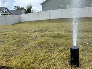 Sprinkler system watering a patchy lawn in a residential backyard, highlighting the importance of irrigation for sod installation.
