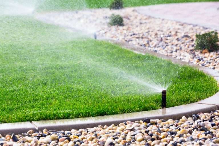 Irrigation system spraying water on lush green lawn with decorative gravel border, enhancing landscape beauty for outdoor spaces.