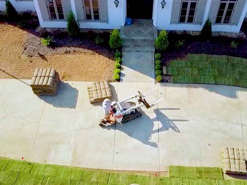 Sod installation process at a residential property in Taylors, SC, featuring a worker operating machinery with sod rolls stacked nearby.