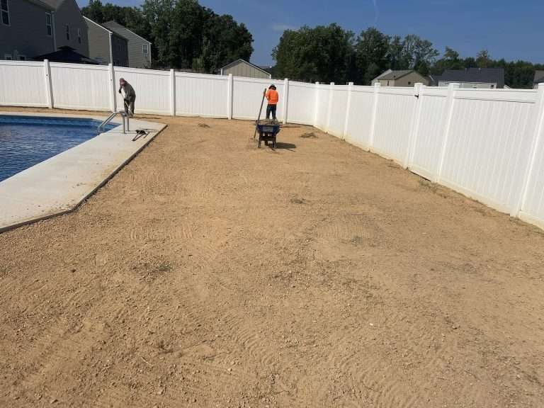 Workers preparing a bare yard for landscaping near a swimming pool, showcasing soil leveling and site preparation for sod installation.