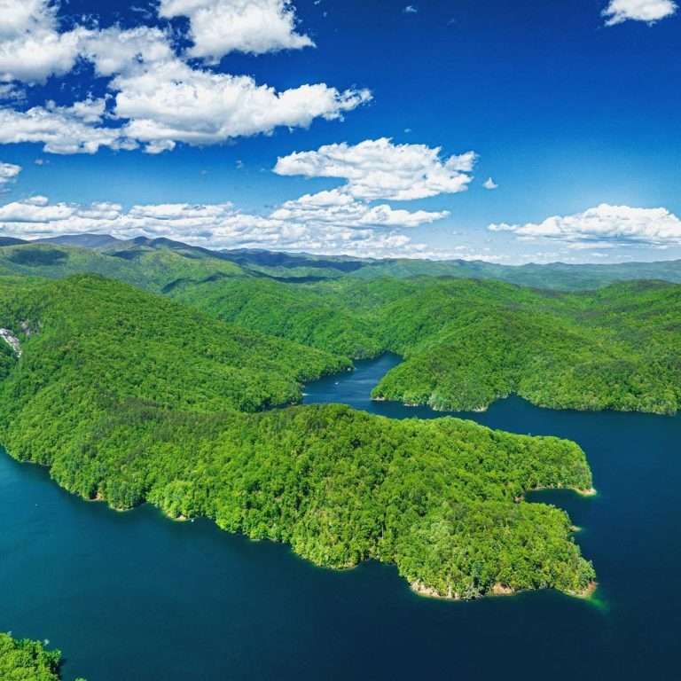 Aerial view of Lake Jocassee surrounded by lush green hills and a clear blue sky, highlighting the natural beauty of the area, relevant to sod installation services offered by Sod Pros Landscaping.