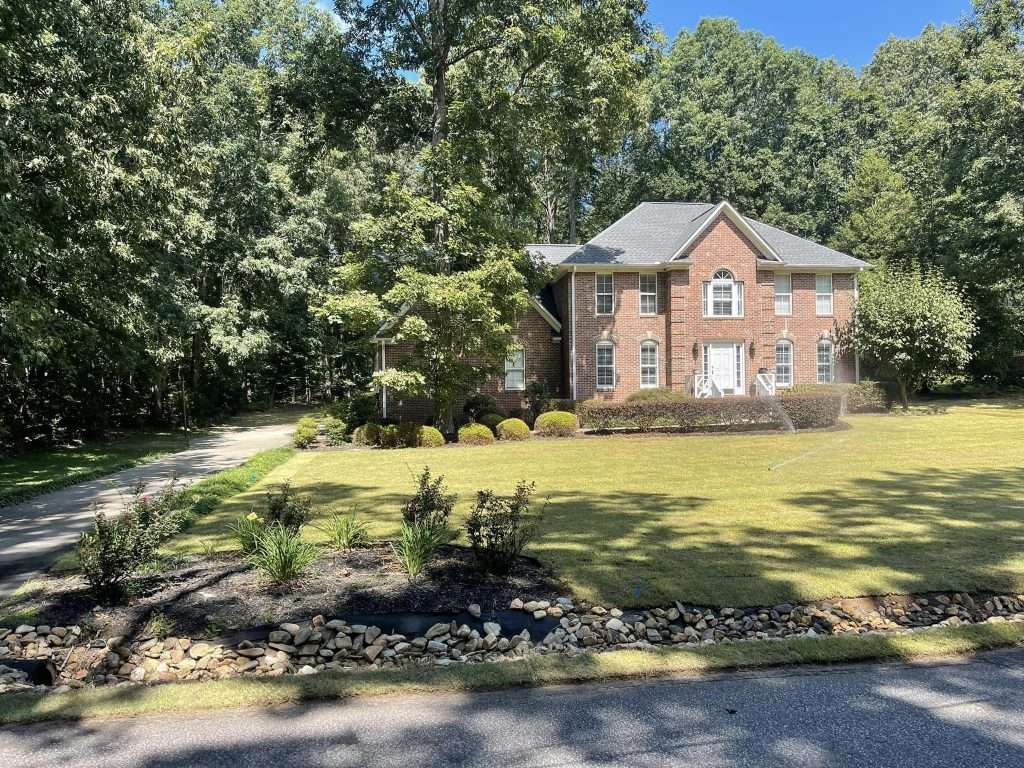 A beautiful brick house with a well-maintained sodded lawn surrounded by trees.